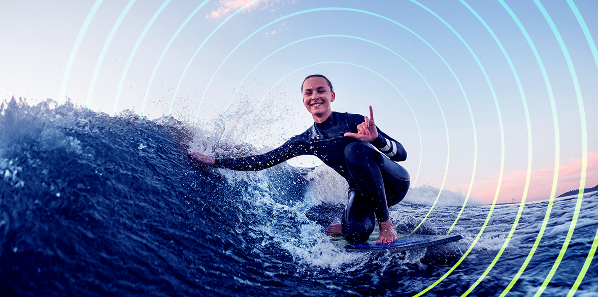 Woman on surf board catching a wave while making hand gesture.